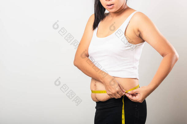 亚洲母亲用剖腹产后疤痕测量腰围、松驰、下腹皮肤、妊娠期脂肪、分娩时与白色背景隔离、健康的腹部多余的身体概念