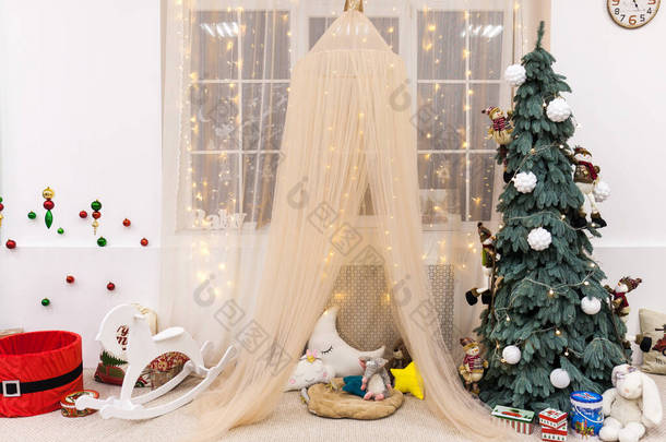 现代室内设计儿童房，大窗户，圣诞和新年装饰，帐篷，玩具，礼物，树，摇曳的马。寒假的构成.