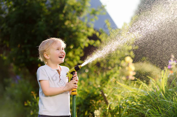 在阳光明媚的<strong>后院</strong>玩花园软管的滑稽小男孩。学前儿童玩喷雾水的乐趣。儿童夏季户外活动.