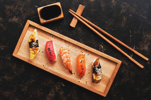 各式寿司设置在黑暗的乡村背景下。日本食品寿司在木盘上, 酱油, 筷子。顶部视图。寿司乌纳吉, 赛克, 马古罗, 埃比.