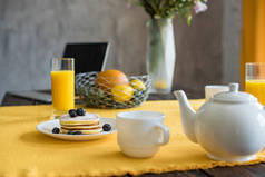 在桌上放上黄色桌布的煎饼、茶杯和果汁杯的特写图