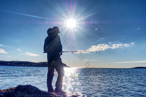 渔夫剪影在日落渔夫检查钓鱼线和推挤诱饵在标尺