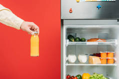 人在开着的冰箱边拿着一瓶果汁，架子上挂着用红色隔开的新鲜食物，这种景象被剪下来了