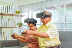 一对年长的亚洲夫妇正在玩电子游戏，还戴着VR护目镜，以适应退休科技的生活方式.