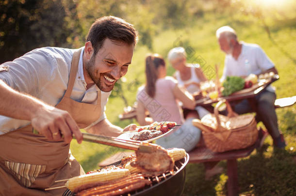 夏天的乐趣。人烹调肉在烧烤为夏天家庭午餐在房子后院.