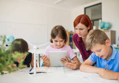 一群小学校的孩子，老师在课堂上围成一圈，使用平板电脑.