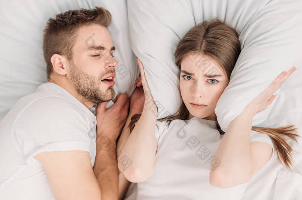 躺在打鼾丈夫身边的女人用枕头塞住耳朵的头像