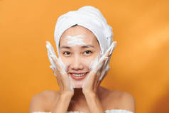 快乐的年轻亚洲女人一边擦面霜一边用毛巾摸脸。孤立的