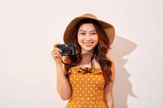愉快的微笑的年轻女子的肖像拍照与灵感和穿着夏装。拿着复古相机的女孩模特在米色背景上在帽子上摆姿势