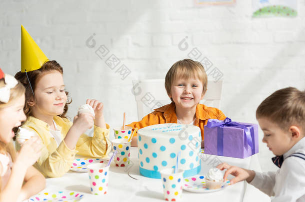 可爱的孩子坐在桌边吃蛋糕在生日派对庆祝活动
