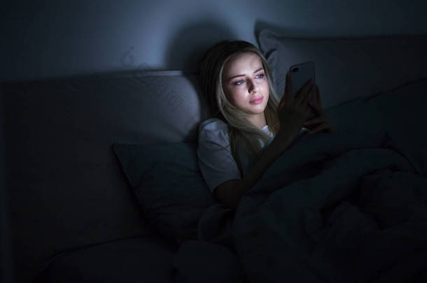 社交网络成瘾，游牧民族恐惧症，失眠，睡眠障碍的概念。女人<strong>沉迷</strong>于24 / 7连接互联网的智能手机，深夜躺在床上用智能手机.  
