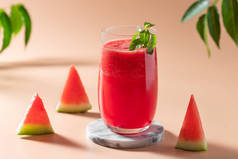 夏天西瓜在玻璃杯中光滑，西瓜片和绿叶在背景中。健康清爽的饮料。米色背景