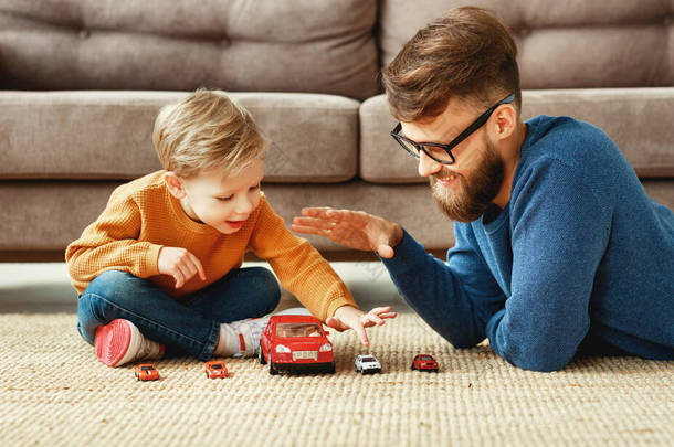 正面的年轻大胡子男子和小儿子坐在沙发旁边的地板上玩着玩具车，在客厅里共度时光的侧影