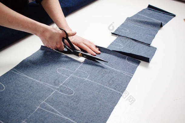 女裁缝用白色桌上的剪刀剪牛仔裤面料的手