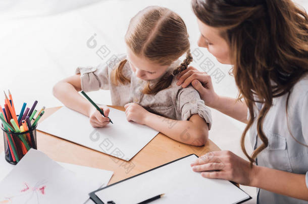 心理学家的高角度的看法与剪贴板坐在小孩附近, 而她用<strong>彩色铅笔画</strong>