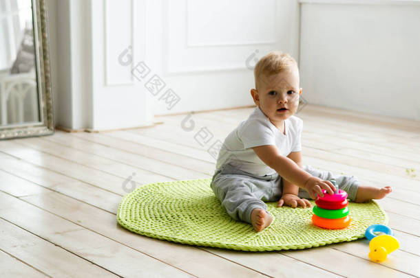小男孩在室内木制地板上的编织地毯上贴着玩具金字塔。在室内编织风格。<strong>温暖</strong>和<strong>舒适</strong>。爱玩的孩子.