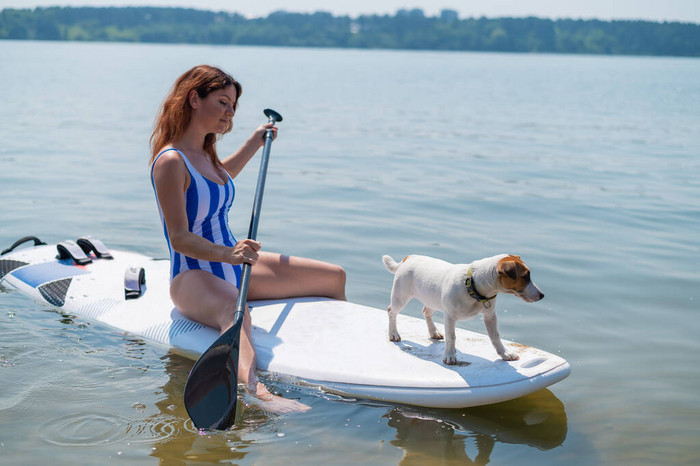 一个女人带着一只狗在湖面上坐冲浪板这个女