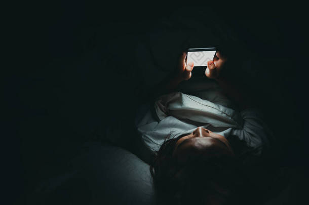亚洲女人晚上在床上玩智能手机，泰国人，<strong>沉迷</strong>于社交媒体