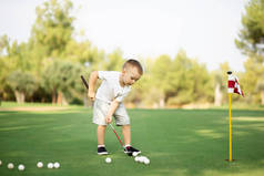 小男孩打高尔夫，在绿草上推杆打球.