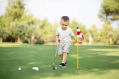 小男孩打高尔夫，在绿草上推杆打球.