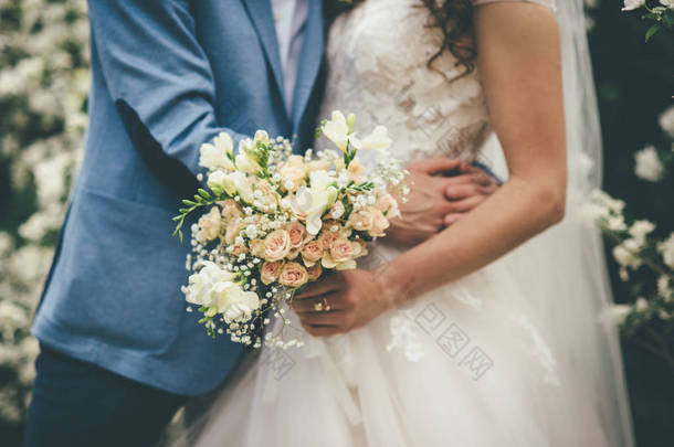 在手中的新郎在婚礼当天的婚礼花束。新婚夫妇拥抱