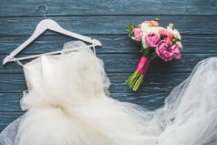 在木质深蓝桌面上的婚纱花束和白色礼服的顶级视图