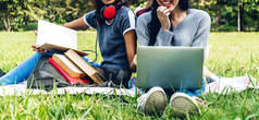 一群微笑的国际学生或青少年坐在一起，用笔记本电脑和书本一起在大学的公园里做作业。教育和友谊的概念