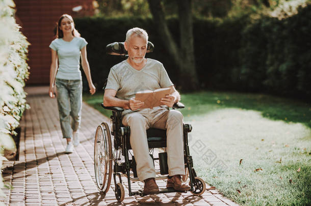 与老人和家庭的康复。商人退休在轮椅上。女人用轮椅帮助老人。年轻的女孩帮助婴儿车。与家庭和轮椅同行。护士帮助与婴儿车.