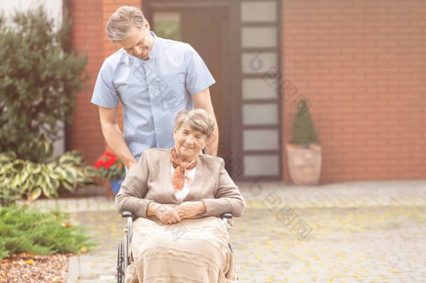 在养老院花园里坐在轮椅上的微笑的英俊男护士和高级退休人员