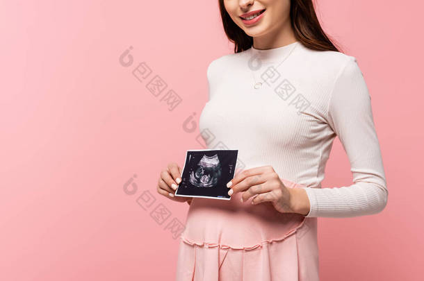 <strong>快乐</strong>的年轻漂亮的孕妇拿着用粉红隔离的超声波扫描的剪影