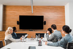 年轻的多文化商人坐在会议室里，凝视着墙上的国际屏幕 