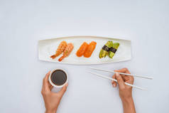 手持筷子和碗酱油的人在吃白色的寿司时被裁剪的镜头
