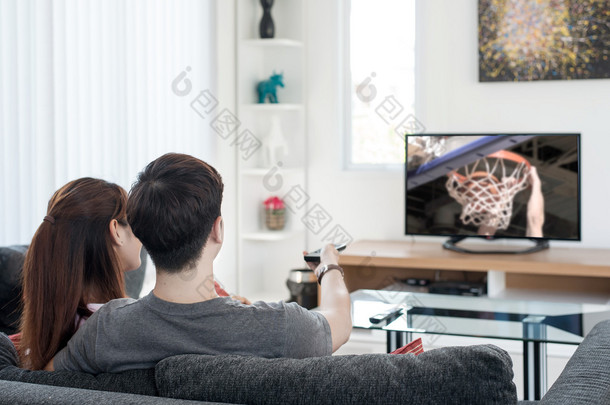 篮球运动电视上观看比赛在家对亚洲年轻夫妇.