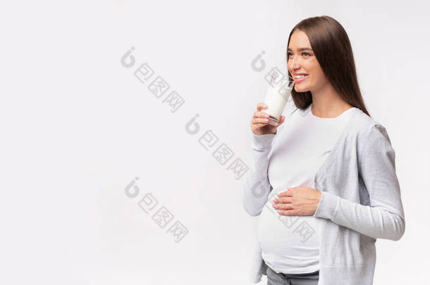快乐怀孕女孩在灰色工作室的背景下喝牛奶，全景