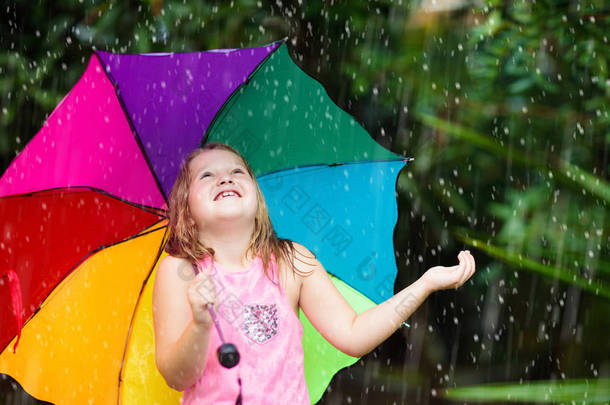 孩子在雨中玩耍。孩子们穿着雨伞和雨靴在外面大雨倾盆地玩耍.小女孩在泥泞的水坑里跳跃.孩子们被秋天的雨天逗乐了.在热带风暴中奔跑的儿童.