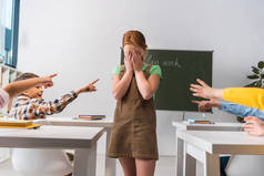 残忍的男生在课堂上用手指指著在同学身边沮丧的同学，欺负的概念 
