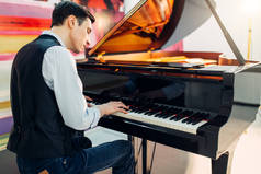 男钢琴家在古典黑色大钢琴, 演出在演播室。音乐家演奏旋律在皇家键盘, 乐器
