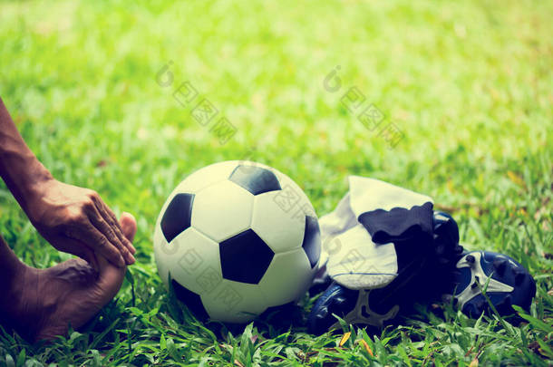 足球和运动鞋在绿草上,<strong>足球运动</strong>员脚痛.<strong>足球运动</strong>员因为脚踝受伤而坐在那里.运动伤害的概念.