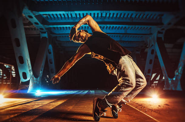 年轻的冷静的人打破舞者在城市桥梁与凉爽和温暖的灯光背景。身体上的纹身.