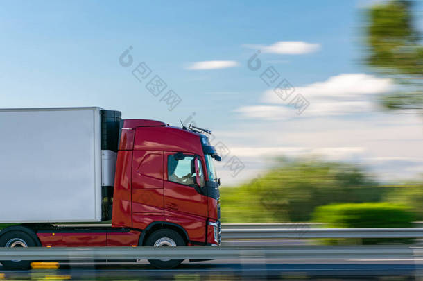 一辆装有冷藏半挂车的<strong>卡车</strong>开在高速公路上，蓝天，乌云密布