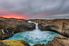 日出时冰岛的阿尔迪耶福斯瀑布, 天空中的金色云朵。惊人的景观在美丽的旅游景点。与冰川水的自然奇迹.