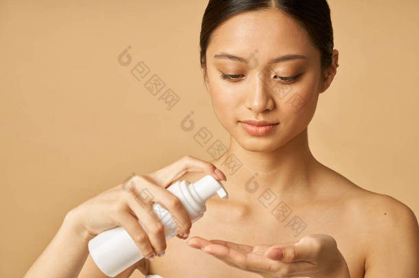 工作室的肖像自然年轻的女人拿着一瓶温和的泡沫面部清洁剂隔离米色背景