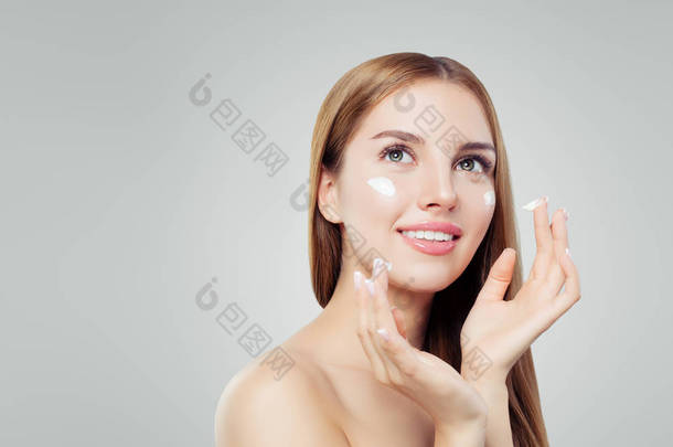 年轻快乐的女人与健康的皮肤应用化妆品霜。护肤、美容和面部护理概念