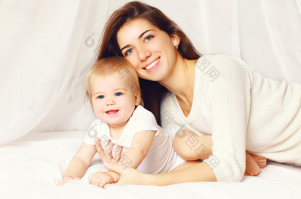 快乐微笑的年轻妈妈和可爱的宝宝，在床上的肖像 