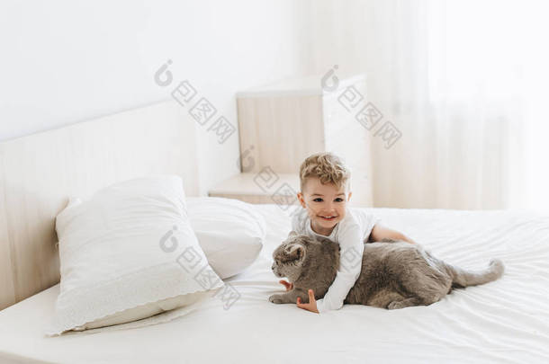 可爱的微笑的孩子玩灰色英国短毛猫在床上在家