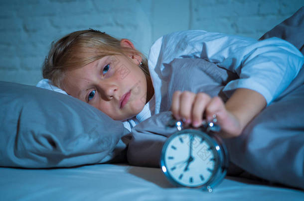 甜蜜的不眠不休的小女孩强调悲伤和愤怒在床上看闹钟不得不醒来, 但感觉不眠不休在麻烦中保持睡眠睡眠障碍和儿童失眠的概念.