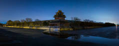 位于中国北京的紫禁城故宫博物馆的西北塔和城墙的全景夜景，反映在半冰冻的护城河上