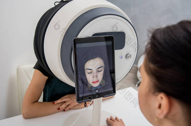 面部皮肤分析系统。 美容师分析女人的脸 现代技术.