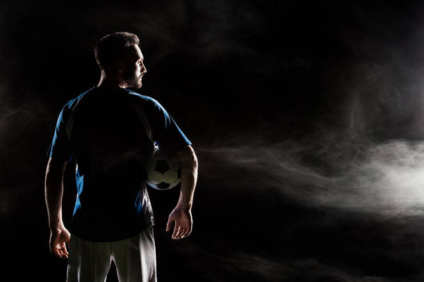 足球运动员的剪影举行球在黑色与烟雾  