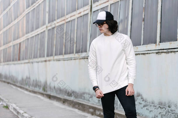 在城市街道上，穿着白色运动衫或帽衫、棒球帽和眼镜的男人。运动衫或帽衫，用于模拟、标志设计或有自由空间的设计印刷品.
